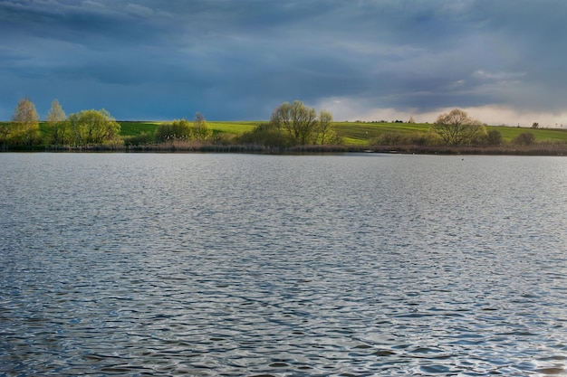 Blick über den See auf die schön beleuchteten Felder im Frühling vor dem Sturmwetter malerische Landschaften