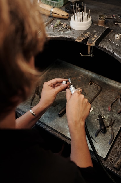 Blick über die Schulter auf einen nicht erkennbaren Juwelier, der in der Werkstatt einen Silberring poliert