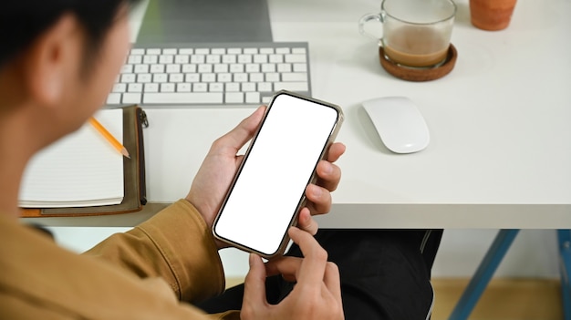 Blick über die Schulter des Geschäftsmannes mit Smartphone am Schreibtisch.