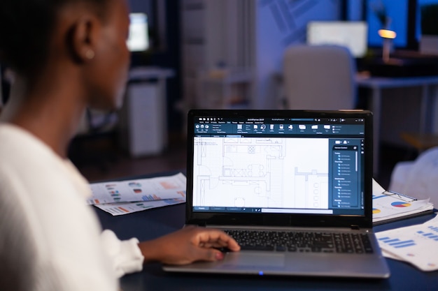 Blick über die Schulter eines afrikanischen Architekten, der spät nachts im Büro mit CAD-Software arbeitet, Hausblaupausen