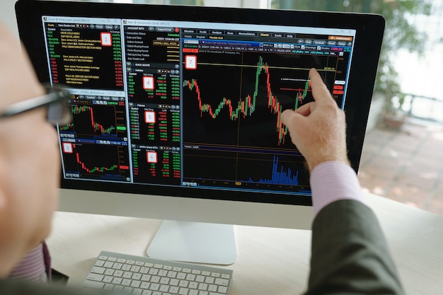 Blick über die Schulter eines Börsenanalysten, der auf den Computermonitor zeigt, während er mit einer bunten Grafik arbeitet