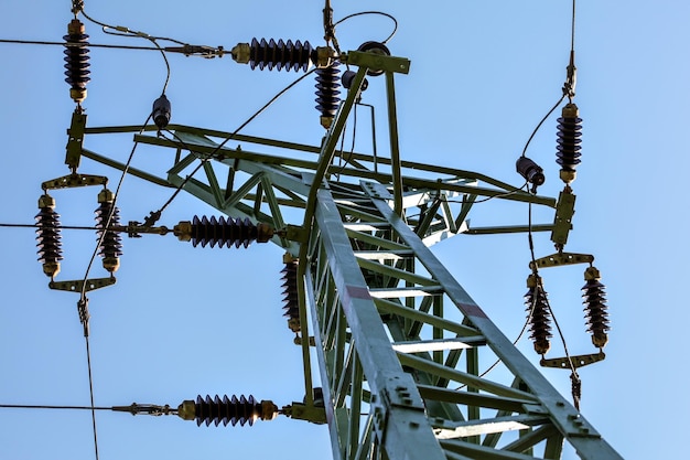 Blick vom Boden bis zur Spitze des Strommastes. Kabel und keramische Isolatoren sichtbar gegen den blauen Himmel. Abstrakter Hintergrund der Energiewirtschaft.