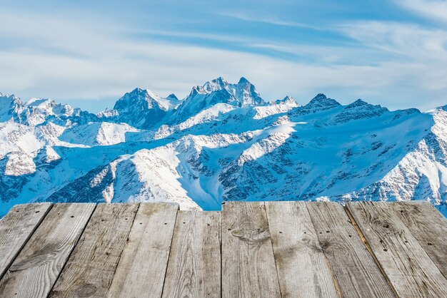 Blick vom leeren Holzdeck auf die sonnigen Winterberge im Bokeh