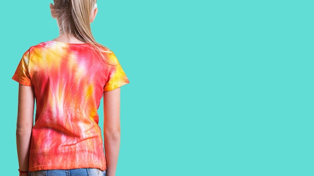 Blick von der Rückseite eines Mädchens in einem T-Shirt im Tie-Dye-Stil auf türkisfarbenem Hintergrund. Weiße Kleidung von Hand bemalt.