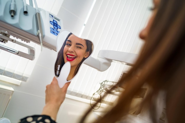 Blick von der Seite einer glücklichen Patientin, die in den Spiegel schaut und ein schönes Lächeln in der Zahnarztpraxis genießt Konzept der Zahnheilkunde und Stomatologie