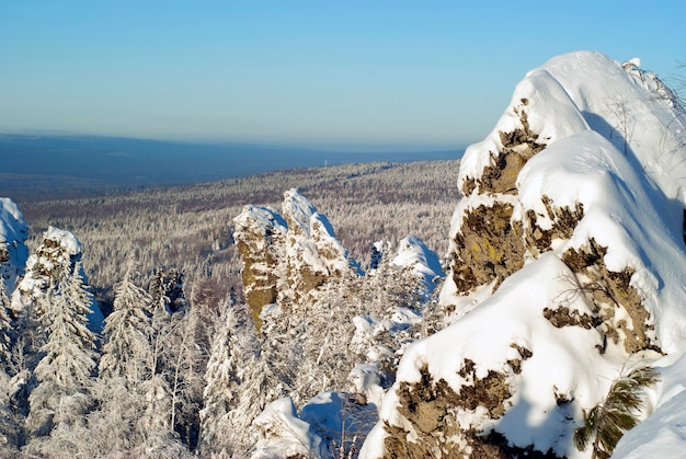 Blick von der Spitze des Uralkamms an einem Wintertag auf bewaldete Hügel und Felsen im Vordergrund