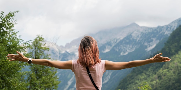 Blick von hinten auf eine junge Frau mit weit ausgebreiteten Armen, die draußen steht