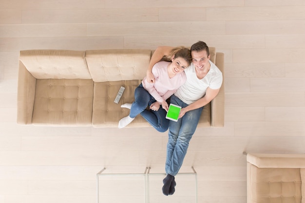 Blick von oben auf das junge Paar, das auf einem Sofa im luxuriösen Wohnzimmer sitzt und einen Tablet-Computer verwendet