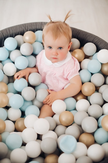 Blick von oben auf das süße kleine Baby, das mit bunten Bällen im Spielplatz-Ballpool im Zimmer spielt. Glückliches Kindheitskonzept