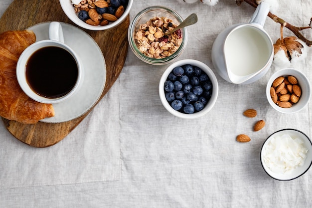 Blick von oben auf den Frühstückstisch mit Kaffee, Croissant, Müsli, Nüssen, Beeren und Milch