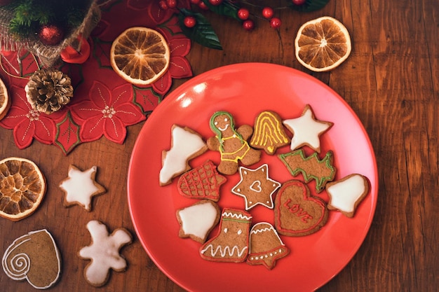 Blick von oben auf den Teller mit hausgemachten Lebkuchenplätzchen auf dem alten rustikalen Holztisch mit weihnachtlicher Vintage-Dekoration im reduzierten Ton