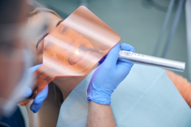 Blick von oben auf die hübsche Frau im Zahnarztstuhl, während der Arzt das Füllverfahren beendet
