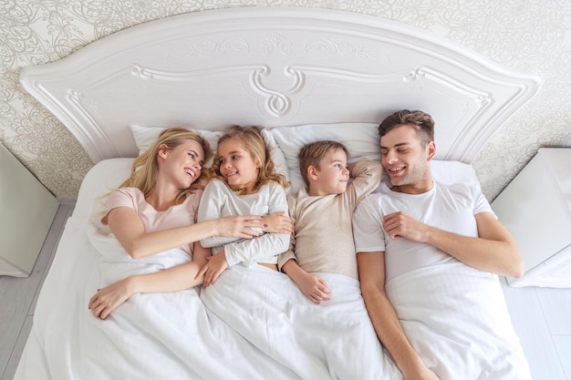 Blick von oben auf die junge Familie, die am Wochenendmorgen zusammen im Bett liegt