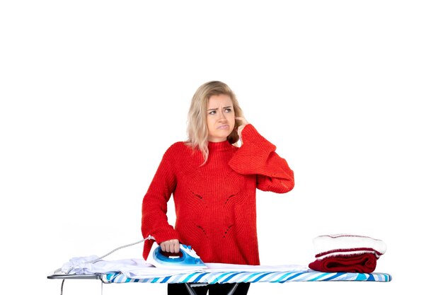 Blick von oben auf die junge und denkende schöne Frau, die Kleidung auf weißem Hintergrund bügelt