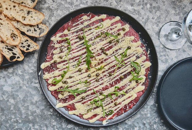 Blick von oben auf die kalte Vorspeise Carpaccio vom Rind mit Parmesan, Kapern und Rucola