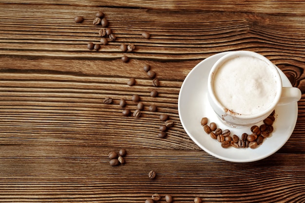 Blick von oben auf die Keramiktasse heißen Cappuccino-Kaffee Latte mit großem schönen Milchschaum, Kaffeebohnen auf Holztisch im Café, Kopierraum.