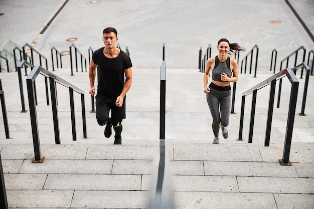 Blick von oben auf die lächelnde schlanke Frau und den athletischen Mann im Outfit, die zusammen zum städtischen Gebäude laufen