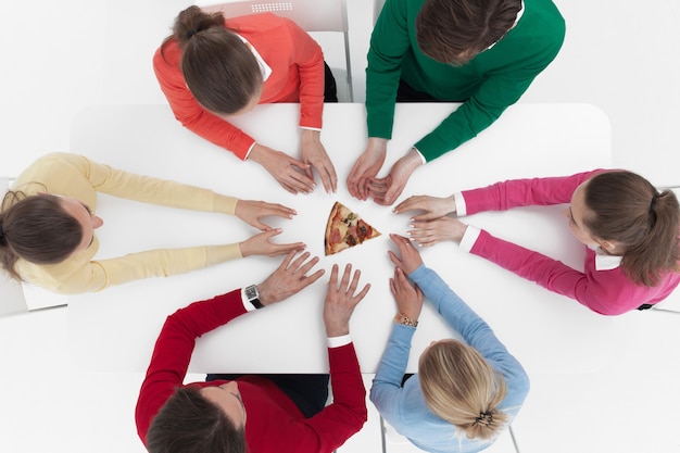 Blick von oben auf die Leute, die um den Tisch herum sitzen und die Hände zum letzten Stück Pizza strecken