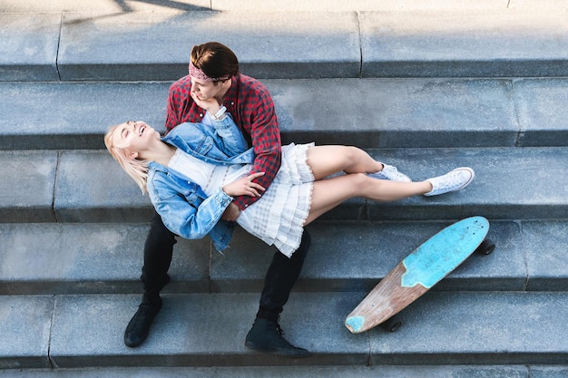 Blick von oben auf ein stilvolles Teenager-Paar mit einem Longboard sitzt auf einer Betontreppe