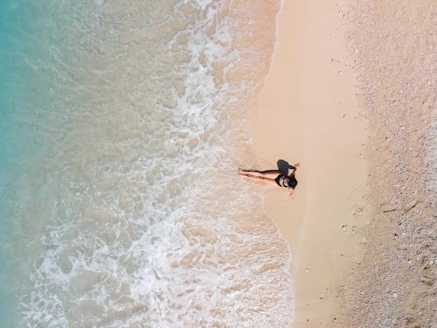 Blick von oben auf eine Frau im schwarzen Badeanzug beim Sonnenbaden am Sandstrand der Küste