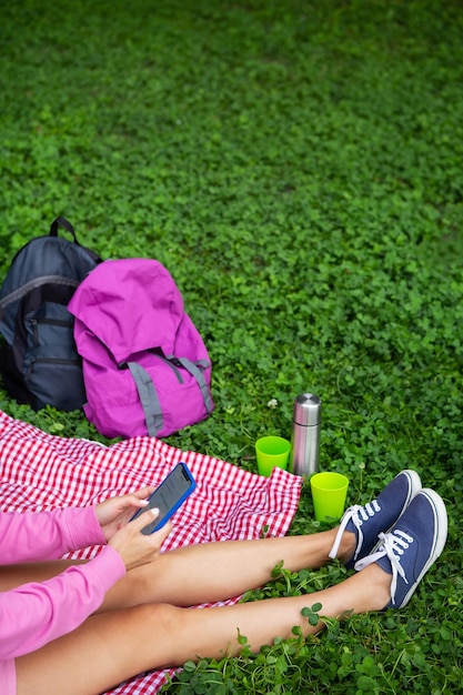 Blick von oben auf eine junge Studentin, die auf einer karierten Decke und grünem Gras im Park sitzt Pause im Freien trinken Kaffee Tee am Telefon sitzen