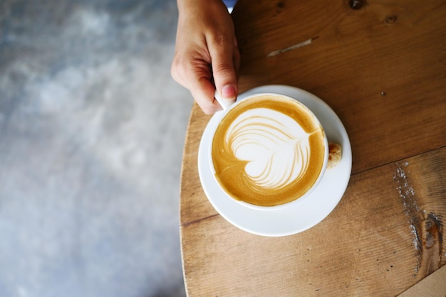 Blick von oben auf eine Tasse Spätkaffee mit herzförmigem Design oben auf dem Café-Tisch