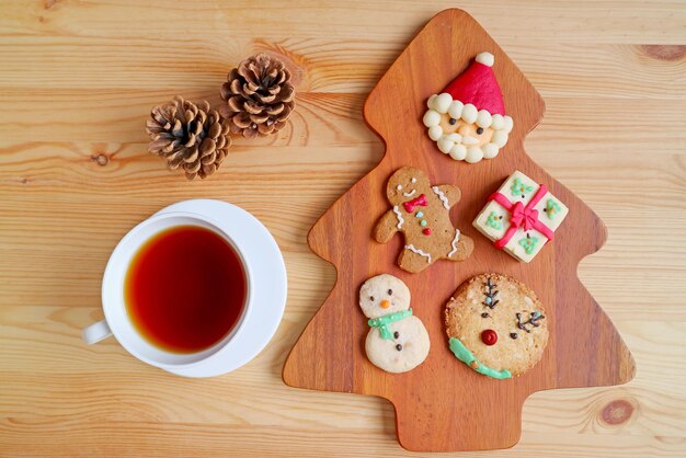 Blick von oben auf verschiedene Weihnachtsplätzchen mit einer Tasse heißem Tee und Tannenzapfen, serviert auf Holztisch