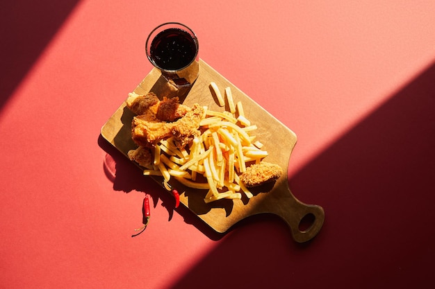 Blick von oben auf würziges frittiertes Hähnchen und Pommes frites, serviert auf einem Holzschneidebrett mit Soda drin