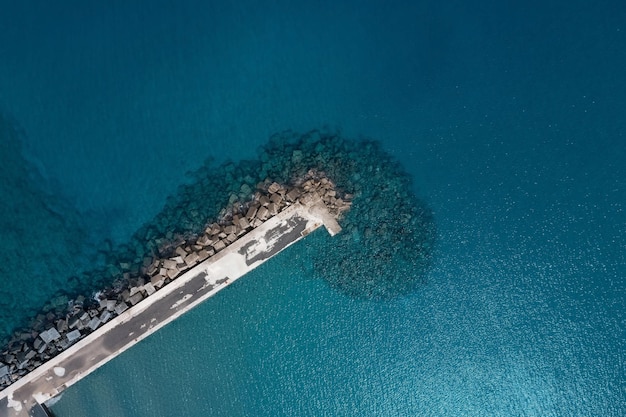 Blick von oben nach unten auf einen langen, schmalen Pier, der sich über klares, türkisfarbenes Wasser erstreckt Kreta Griechenland