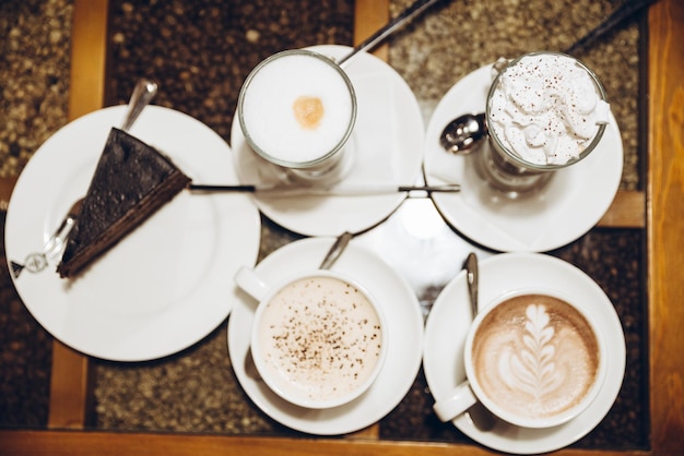 Foto blick von oben vier tassen aufwärmgetränk auf dem tisch mit stück kuchen