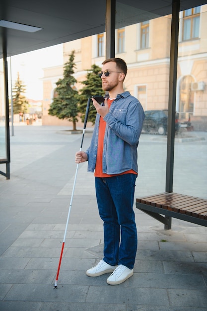 Blinder Mann mit weißem Stock, der auf öffentliche Verkehrsmittel in der Stadt wartet