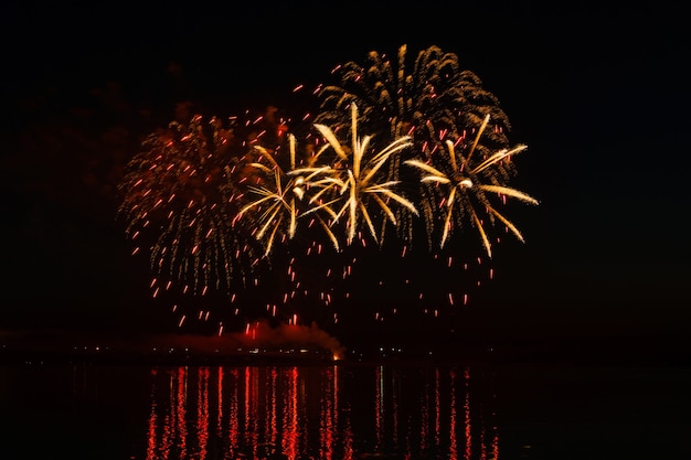 Blitze von festlichem Feuerwerk über dem Nachtfluss spiegeln sich im Wasser