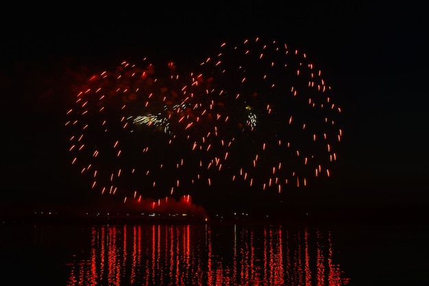 Blitze von festlichem Feuerwerk über dem Nachtfluss spiegeln sich im Wasser