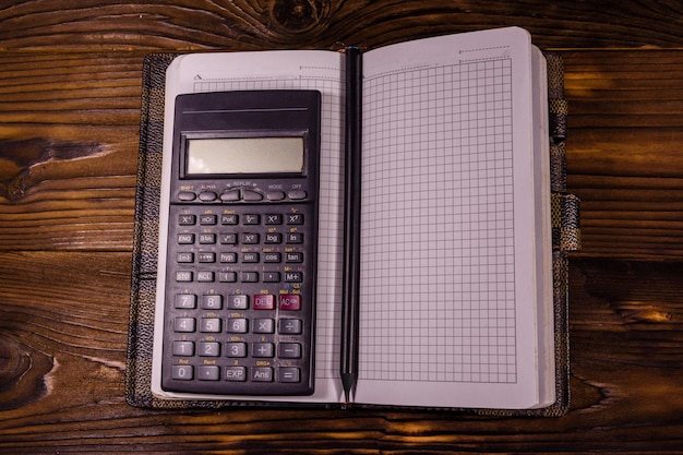 Bloc de notas abierto, calculadora científica y lápiz sobre una mesa rústica de madera. Vista superior