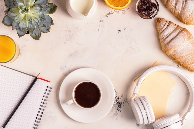 Bloc de notas, auriculares, croissants y café en la mesa blanca.