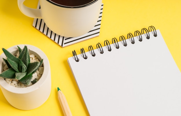 Bloc de notas en blanco de escritorio con espacio para texto. Endecha plana de fondo de mesa de trabajo amarillo con taza de té y plantas.