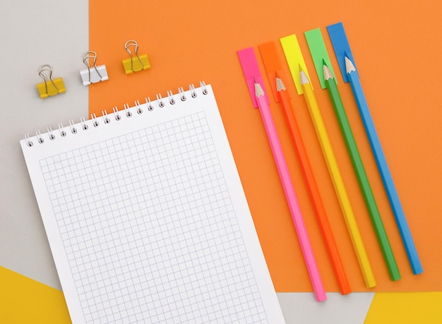 Bloc de notas en blanco lápices de colores y clips de papel sobre fondo de colores