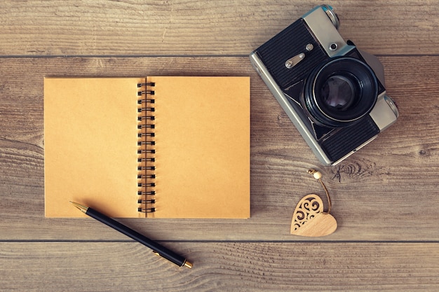 Bloc de notas con bolígrafo y cámara de fotos retro sobre superficie de madera