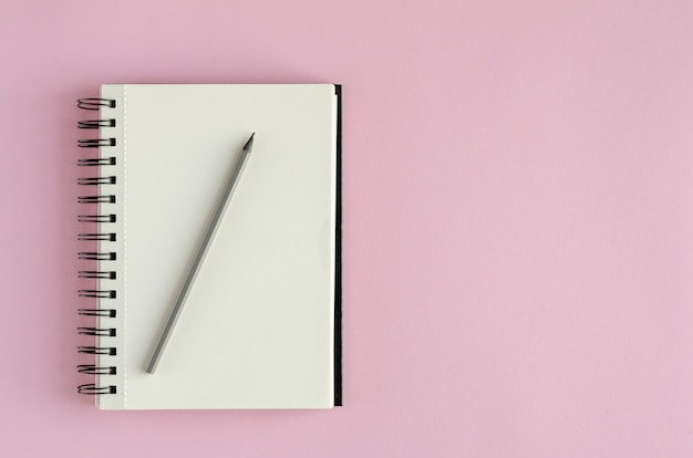 Bloc de notas con composición de lápiz sobre fondo rosa.
