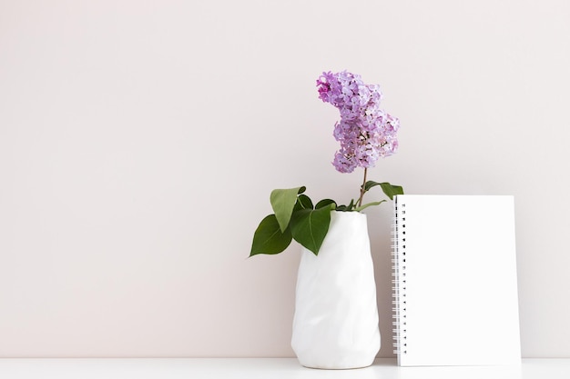 Bloc de notas limpio con flores lilas de primavera sobre fondo blanco de madera