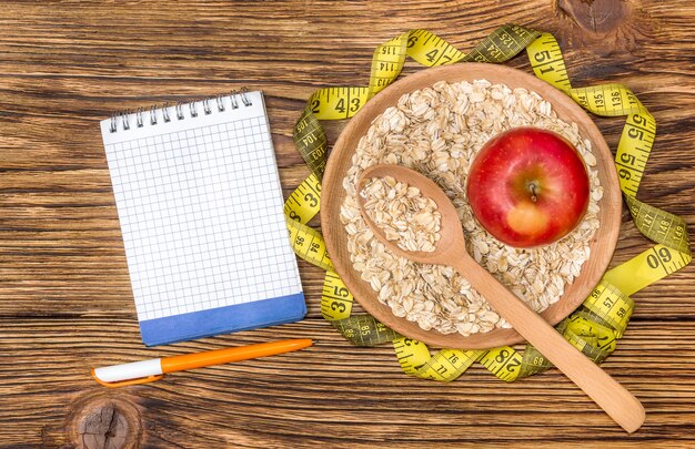 Bloc de notas con manzana, copos de avena y cinta métrica