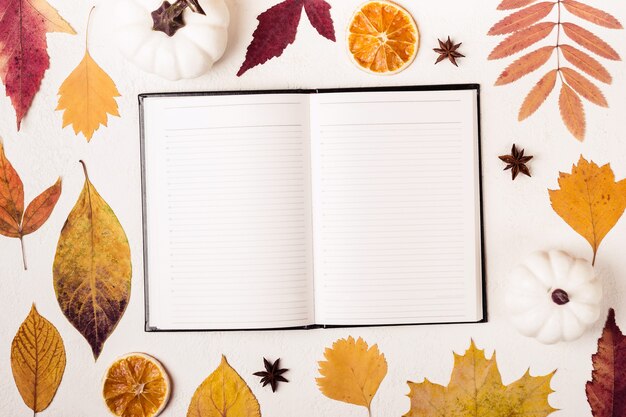 Bloc de notas en la mesa blanca con patrón de hojas de otoño.
