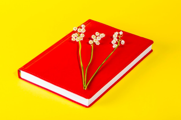 Bloc de notas rojo con flores de lirio de los valles sobre un fondo amarillo