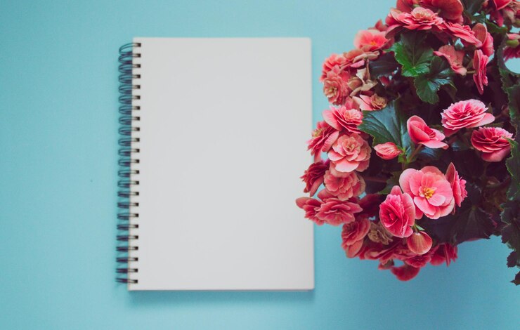 Bloc de notas sobre un fondo azul con flores de color rosa