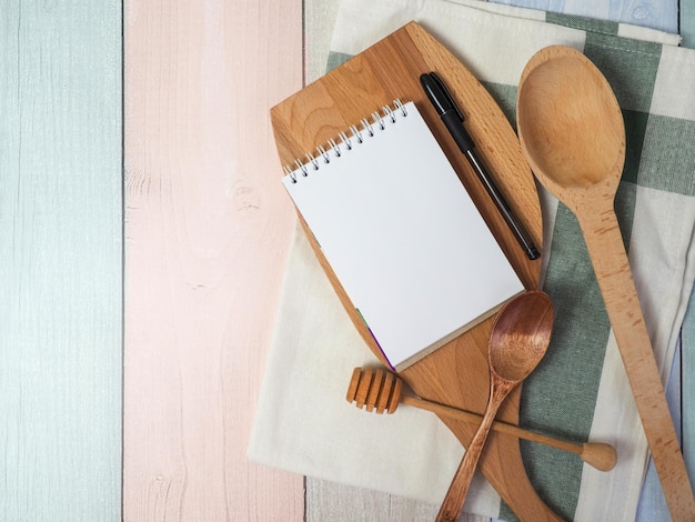 Bloc de notas en la tabla de cortar con utensilios de cocina de madera en el espacio de copia de recetas de comida de mesa