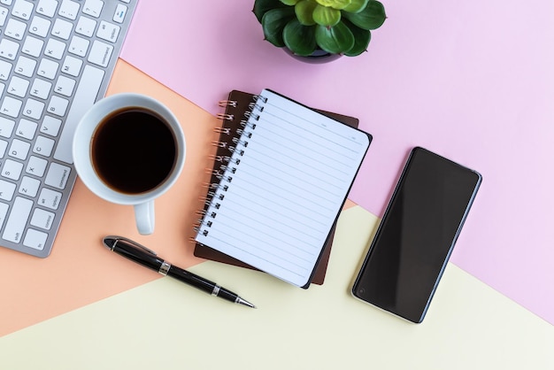 Bloc de notas con taza de café, calculadora, teclado de computadora, planta en maceta y bolígrafo