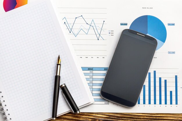 Bloc de notas y teléfono inteligente con gráficos de negocios en la mesa Concepto de negocio