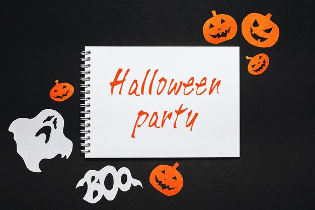 Bloc de notas con texto fiesta de Halloween sobre fondo negro con murciélagos, calabazas y fantasmas