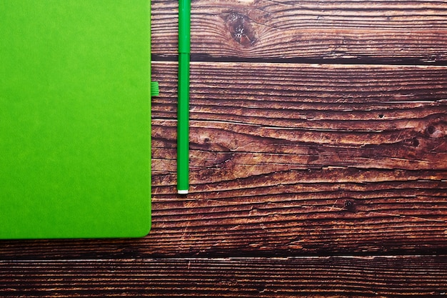Bloc de notas verde con un rotulador sobre una mesa de madera marrón, vista superior.