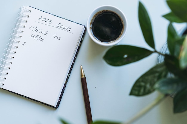 Bloco de notas aberto com resoluções de ano novo de texto e lista vazia Flor e xícara de café no fundo